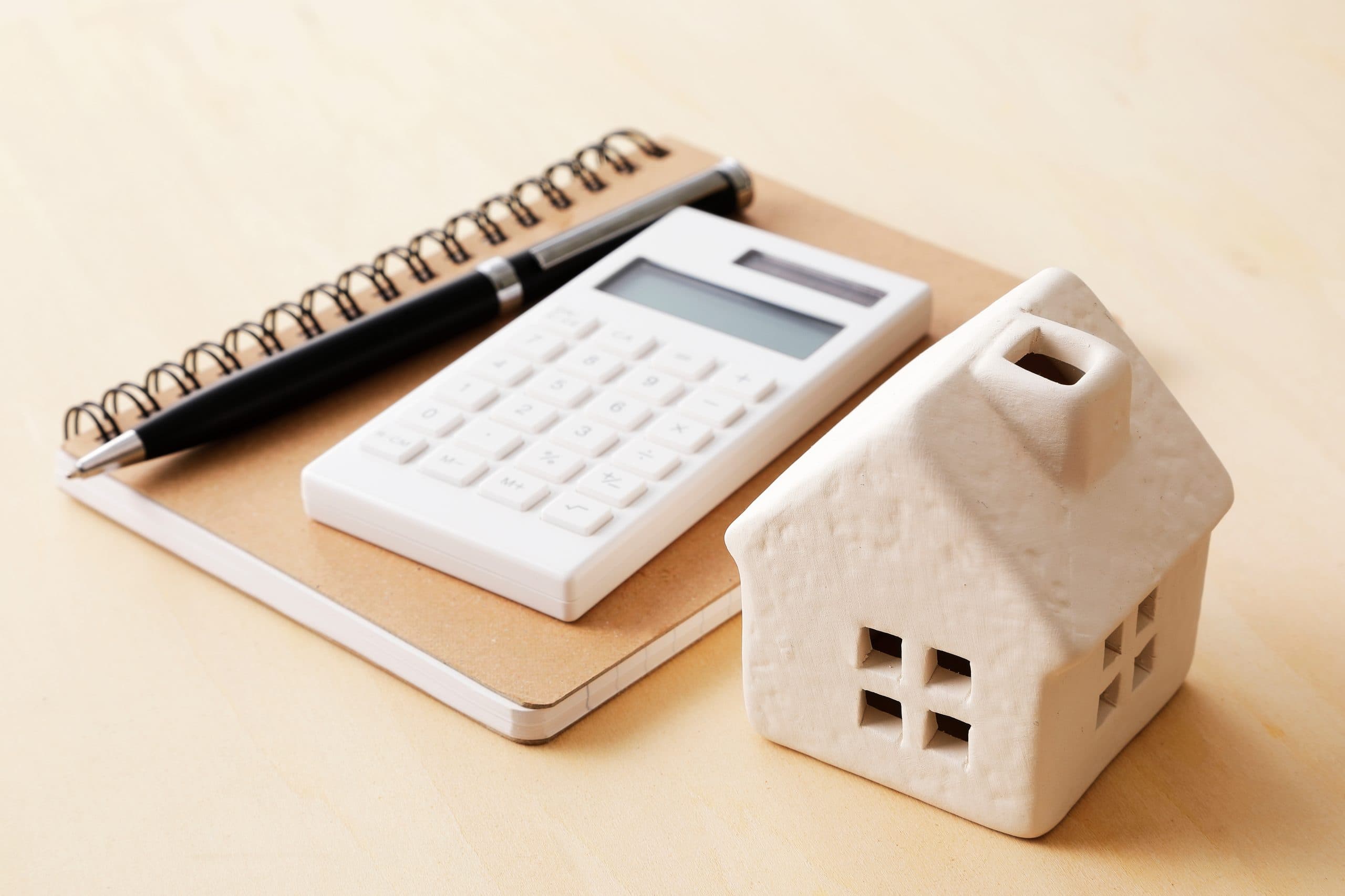 Model house beside a calculator and notepad on a desk during financing planning