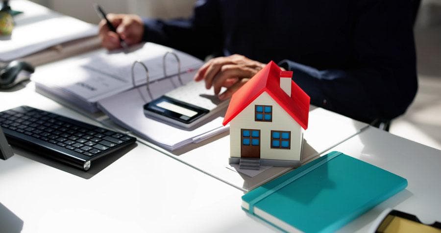 Adviser at a desk with documents, a calculator and a red roofed model house